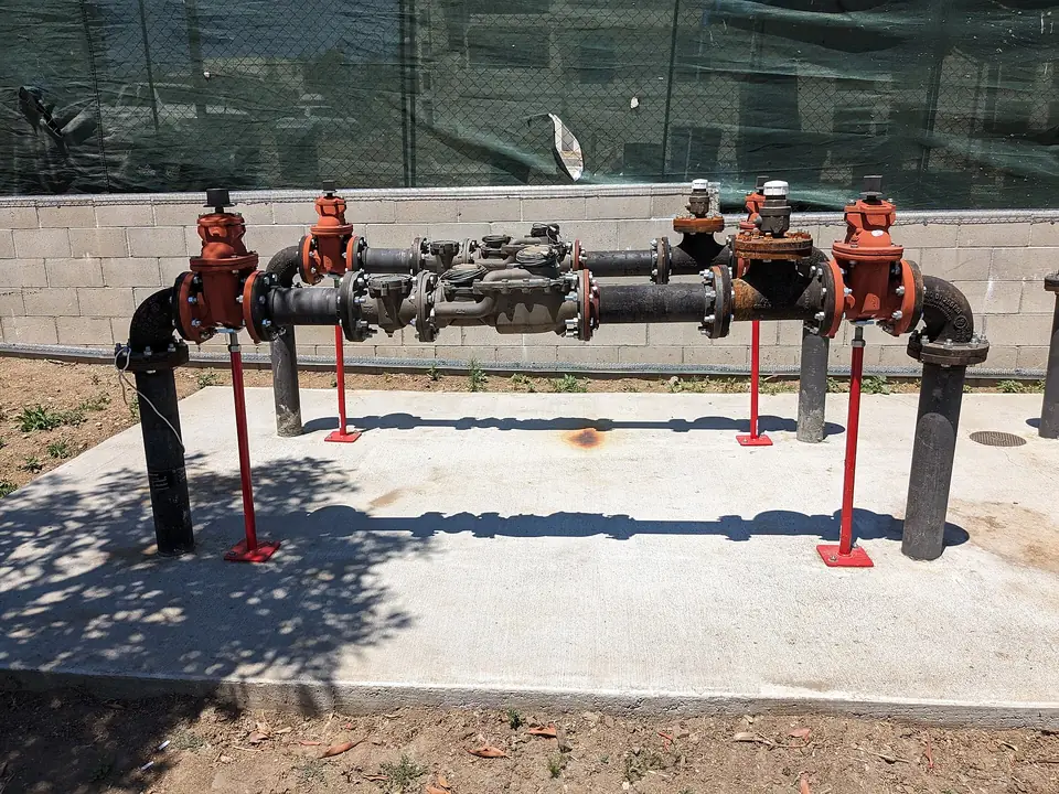 A backflow preventer assembly with red valves next to a water meter