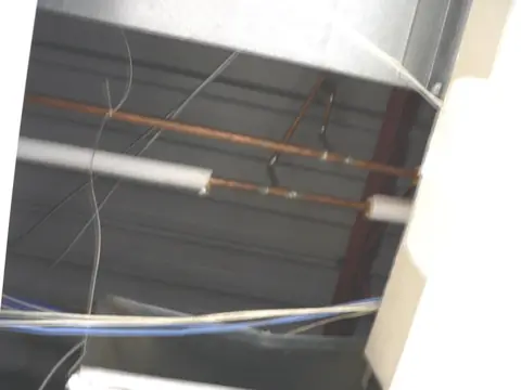 Copper water pipes above a ceiling, one section wrapped in fiberglass insulation and one bare