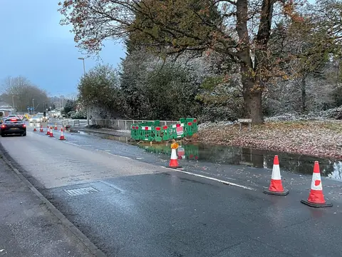 Water from a broken main running along a street with traffic cones