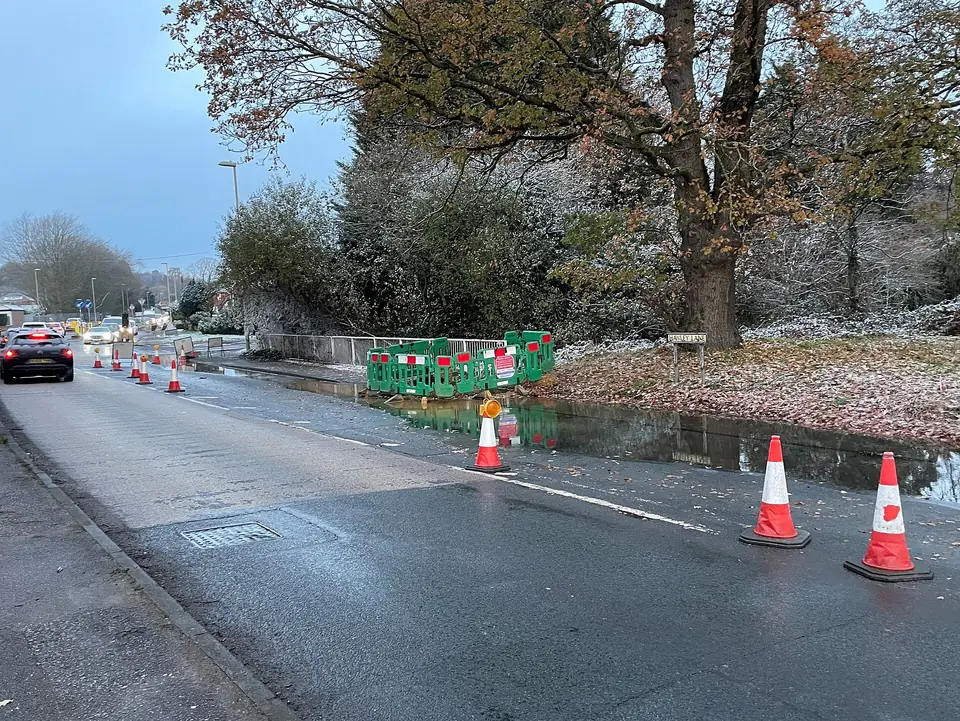 Water from a broken main running along a street with traffic cones