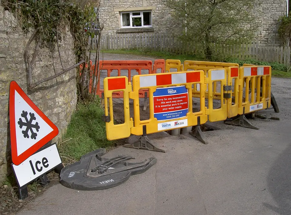Road barriers and an ice warning sign around a water main repair