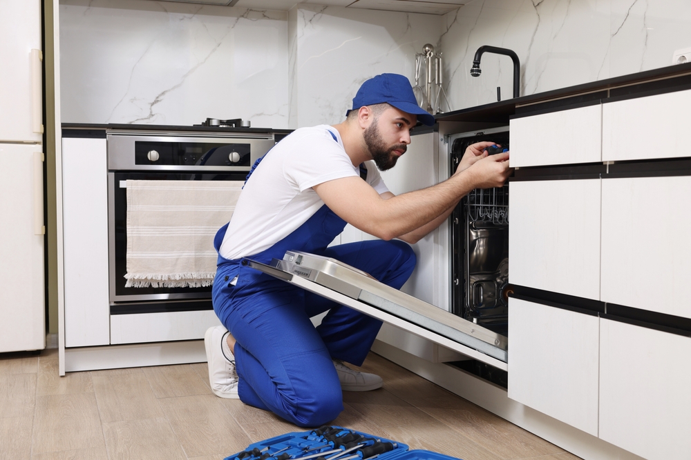 Serviceman,Repairing,Dishwasher,With,Screwdriver,In,Kitchen